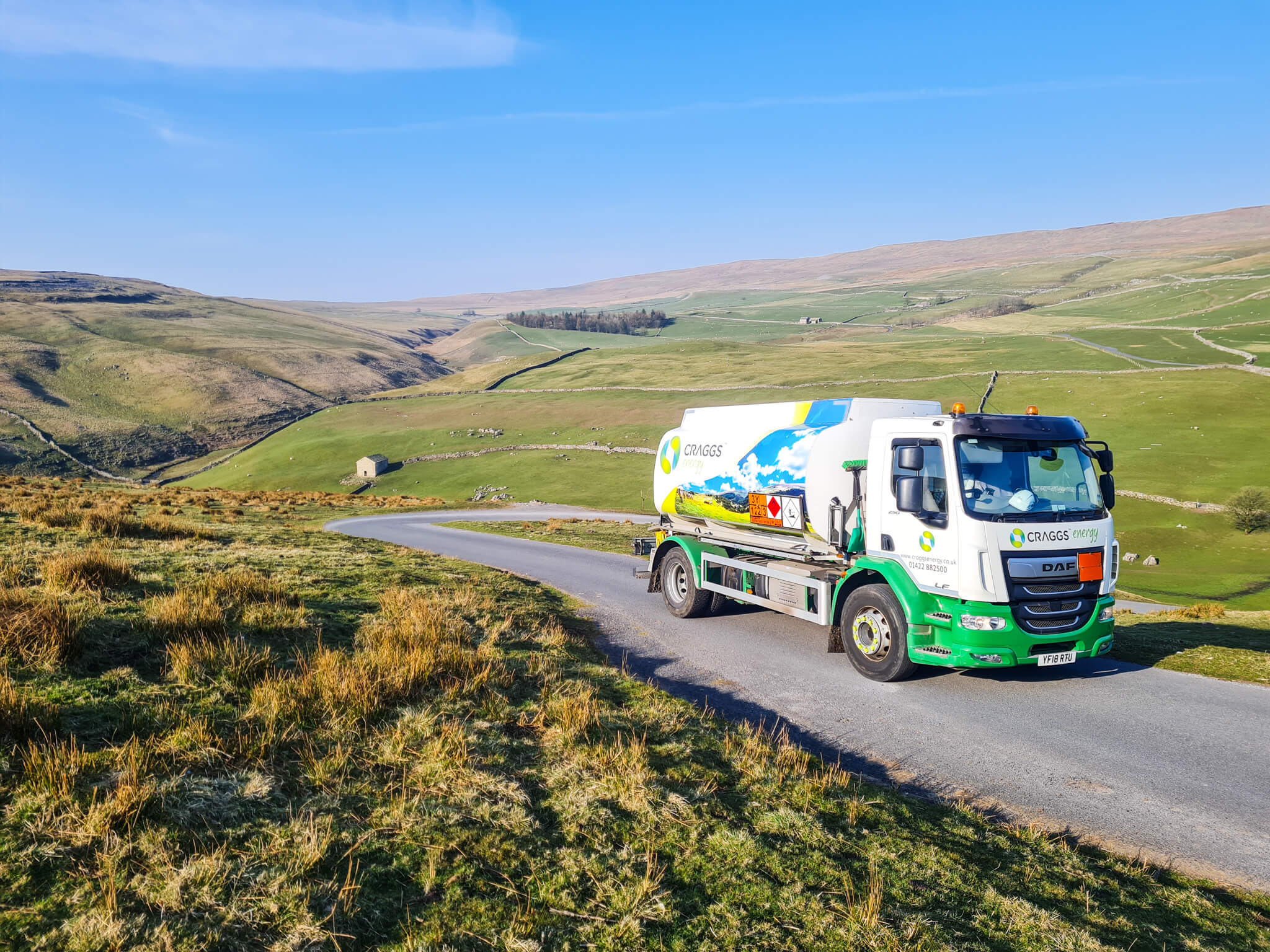 Craggs Energy tanker on a rural road with a home in the background and rolling green hills and a bright blue sky.