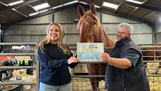 A woman and a girl holding a certificate next to a horse in a rustic stable setting.