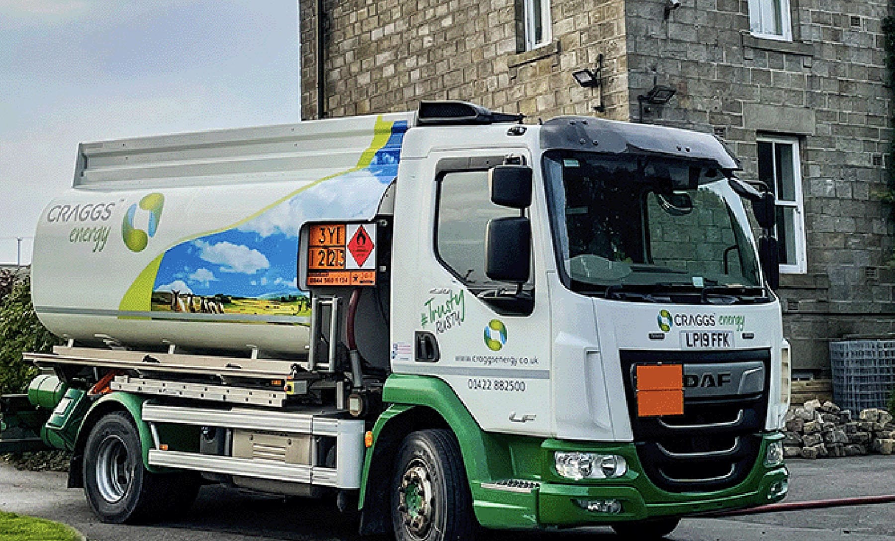 A fuel delivery truck parked on a residential street, featuring a modern design with green and white color scheme and company branding.