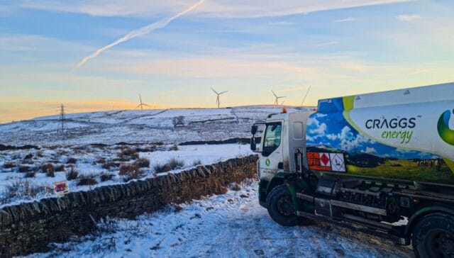 A Cragg's Energy truck parked on a snowy hillside, with wind turbines visible in the background during sunset.