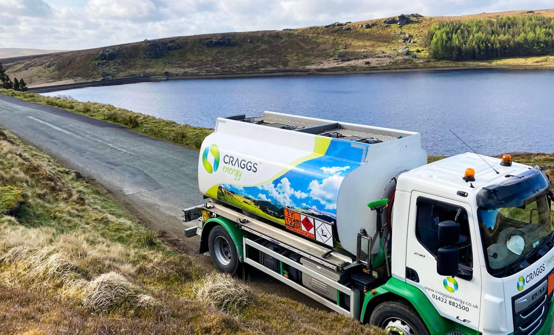 A fuel delivery truck parked near a peaceful lake surrounded by hills and greenery, showcasing a scenic countryside view.