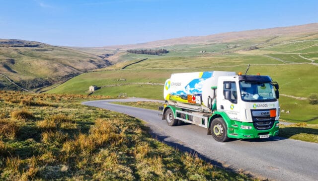 A green and white eco-friendly truck on a winding road surrounded by rolling hills and grassy fields.