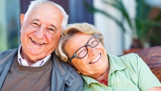 An elderly couple sitting closely together, smiling and enjoying each other's company in a warm, inviting environment.