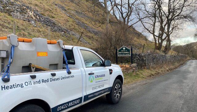 A delivery truck for heating oil and red diesel parked on a rural road with trees and a hillside in the background.
