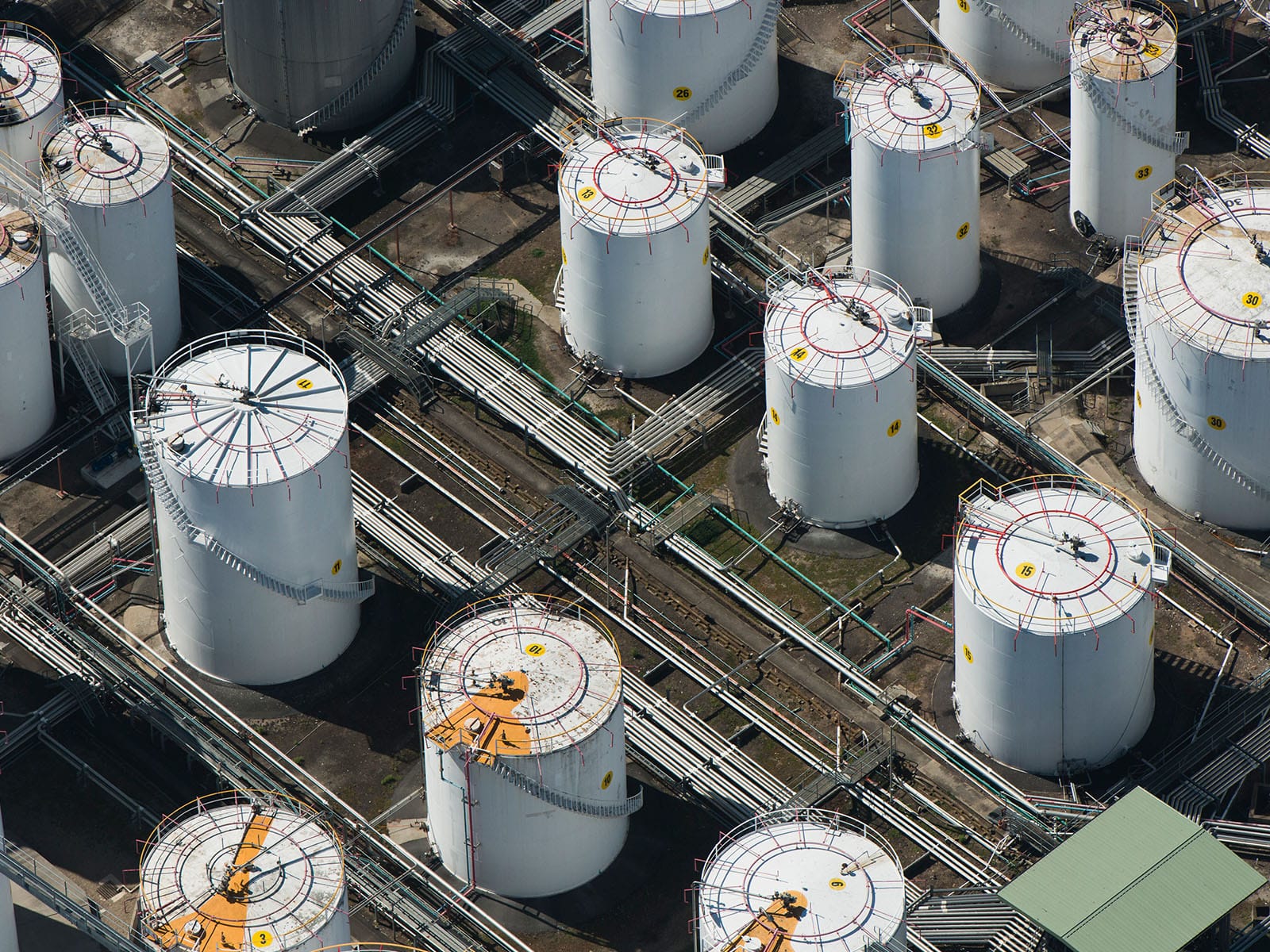 Aerial View of Industrial Storage Tanks An aerial perspective of numerous industrial storage tanks with pipelines and valves visible.